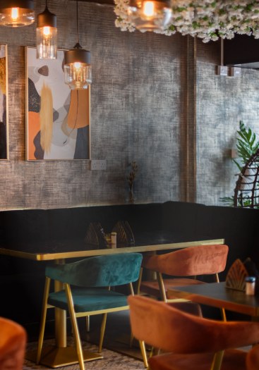 The dining room at ÉKO '77 New Cross — a long table along the banquette with teal and orange velvet chairs