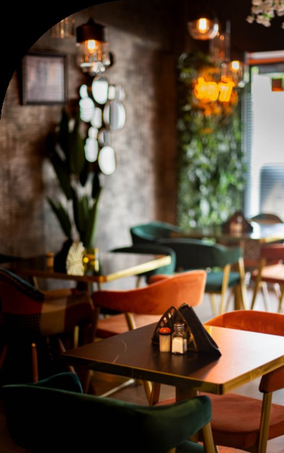 The dining room — green velvet chairs, dark tables and hanging lamps