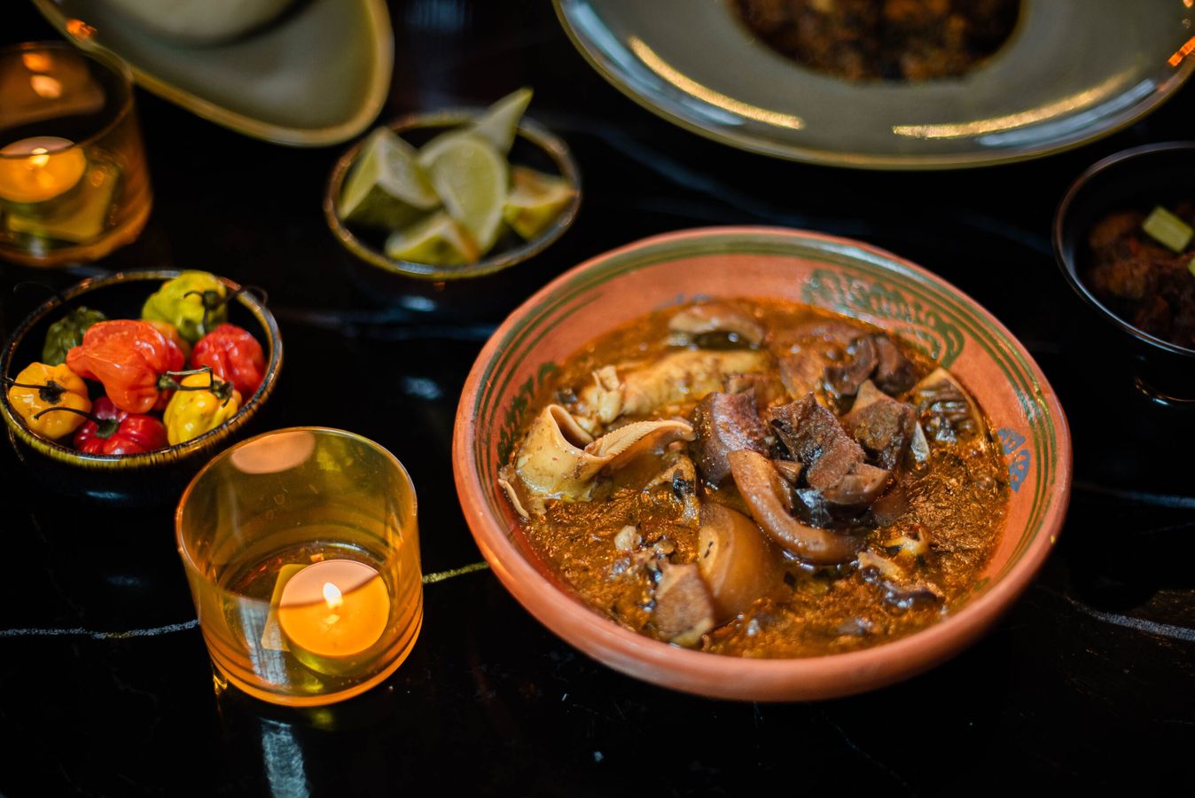 Goat pepper soup in a clay pot, with peppers, lime and a candle
