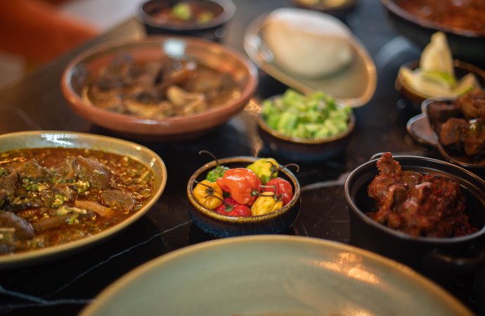 Bowls of pepper soup, greens, scotch bonnets and peppered meat on a dark table