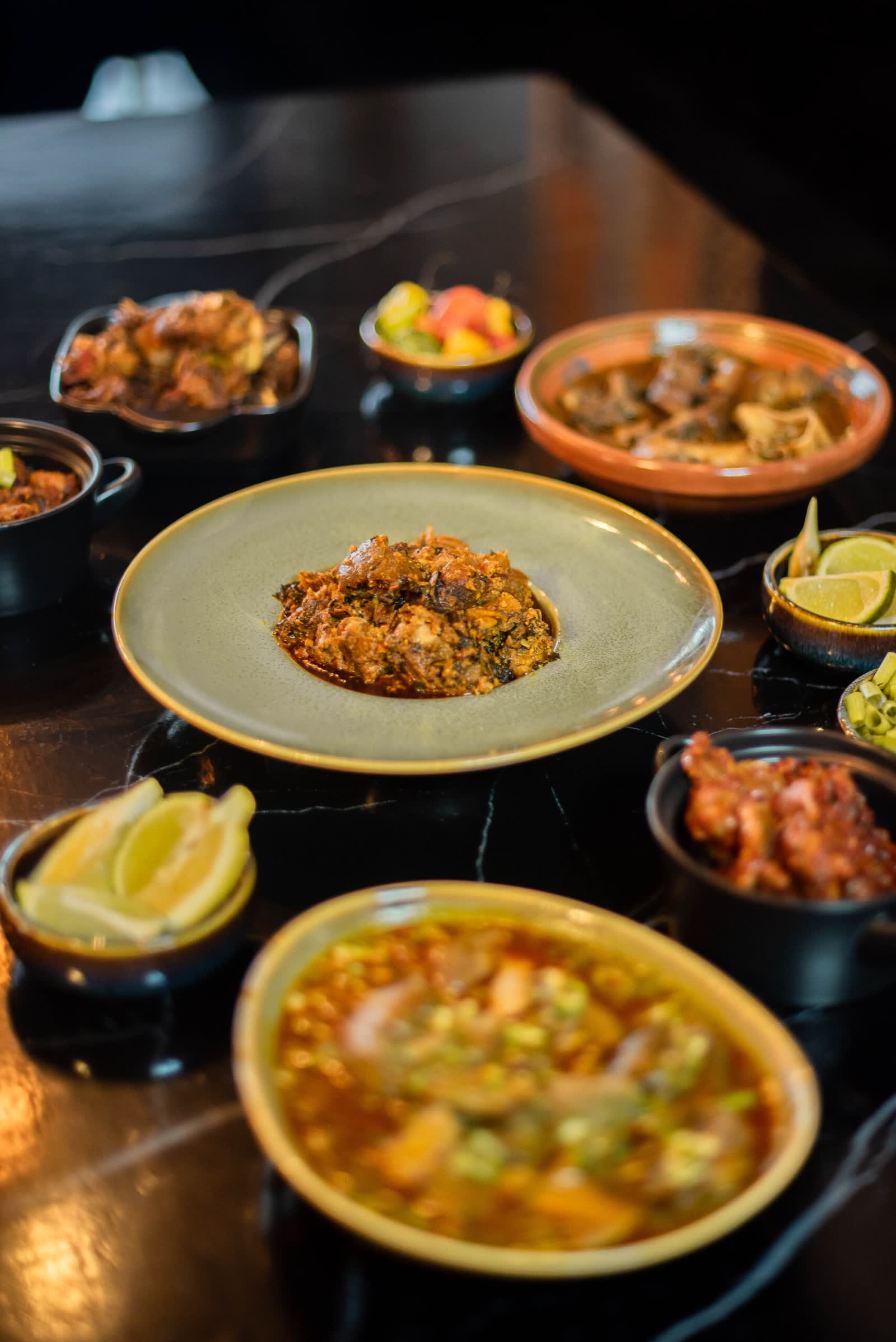 A laid table with terracotta and black bowls, chopped greens and lemon wedges