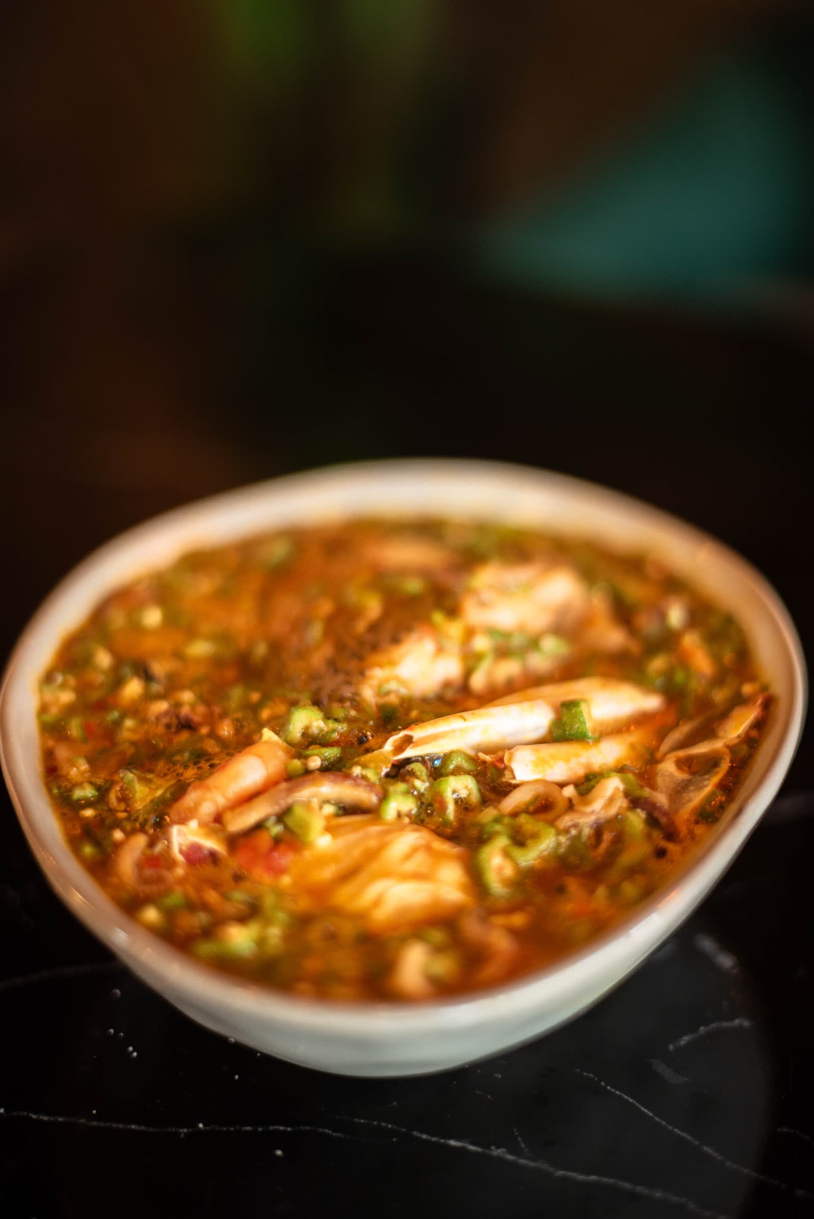 A white bowl of stew with prawns and chopped greens