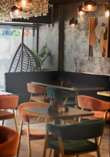 A dining room with a black banquette, terracotta and teal velvet chairs and a hanging egg chair by the window