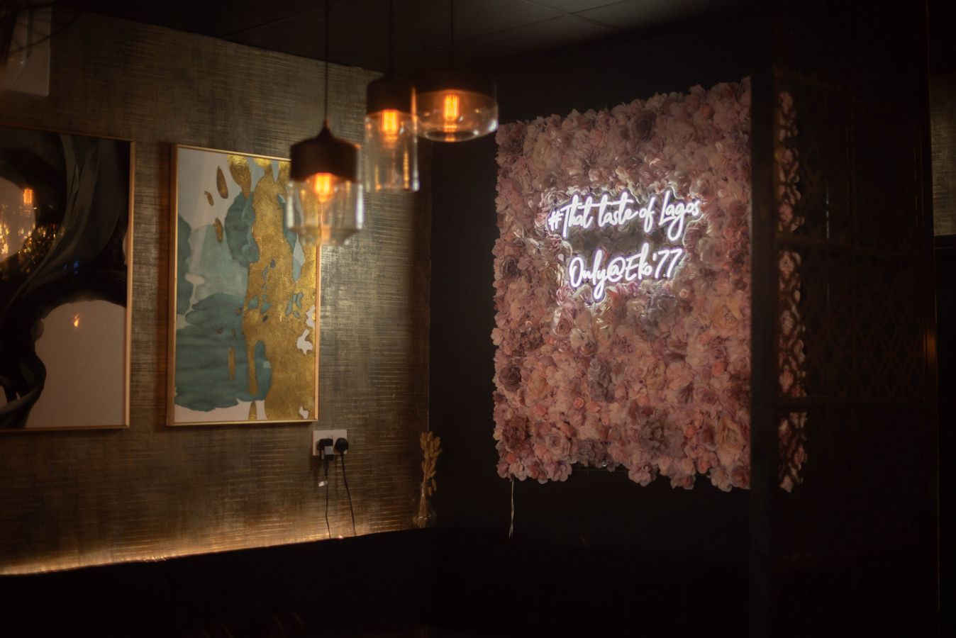 The dining room wall — a flower wall under a neon sign reading The true taste of Lagos