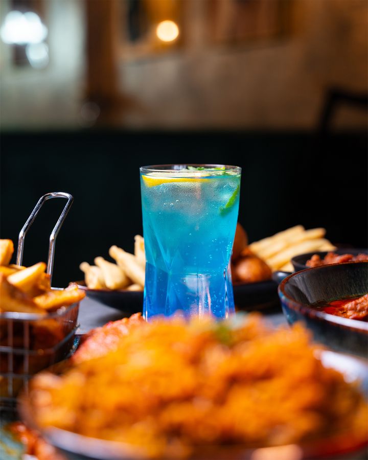 A blue cocktail beside peppered chicken and chips